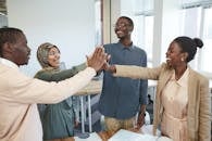 A joyful group of diverse colleagues high-fiving each other in an office, symbolizing teamwork and collaboration.
